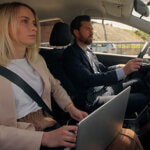 Man driving with woman as a passenger in car holding a laptop computer