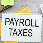 The words, "payroll taxes" in the center of a white notebook resting on another notebook