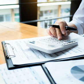 Hand of person holding a pen and typing on a calculator on top of a clipboard