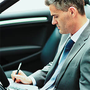 Businessman sitting in his car, he is planning and scheduling meetings on his organizer and using apps on his smartphone