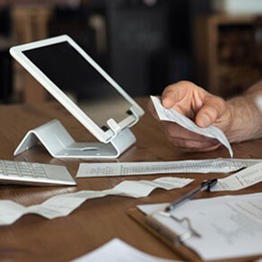 Tablet propped up surrounded by receipts and hand holding a receipt