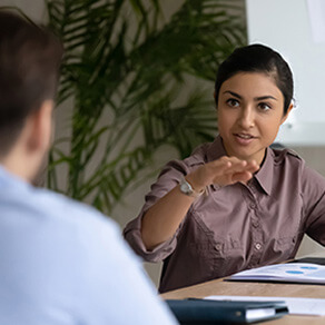 Woman seated at a table speaking to man, only see back of man