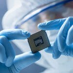 Scientist fully dressed in medical scrubs looking closely at a computer chip