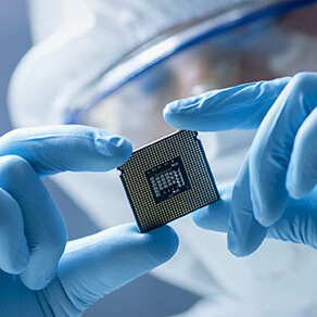 Scientist fully dressed in medical scrubs looking closely at a computer chip