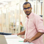 Man standing at a table with papers laid out in front of him and a pen in his hand