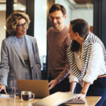 Group of coworkers smiling, in conversation and looking over documents