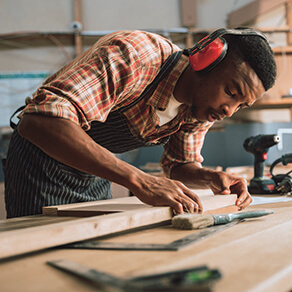 Man, wearing noise cancelling headphones, working on a project at wood working bench