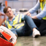Selective focus at hat, Men worker feel painful and hurt from the accident that happen inside of industrial factory while his co-worker come to give emergency assistance and help. Accident in factory.