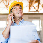 Senior architect with smartphone at the construction site.