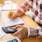 Person working at a desk with pencil, paper and a calculator