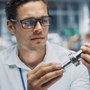 Close Up Portrait of Young Engineer in Glasses Working on Manufacturing Metal Parts