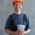 A happy worker in a protective helmet holding cash