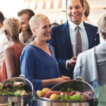 Man and woman standing with group of people in front of food at a professional event