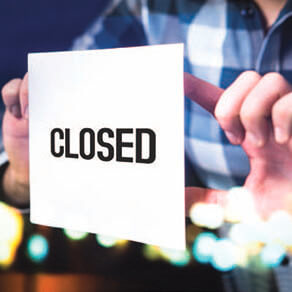 Person holding up sign reading “CLOSED”