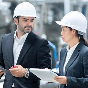 Two manufacturers on a job site dressed in suits and hard hats reviewing documents