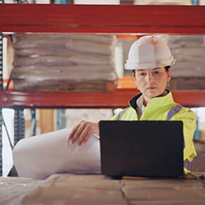 Woman on laptop in warehouse typing up report
