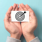 A pair of hand cupped together holding a small target symbol with an arrow in the middle