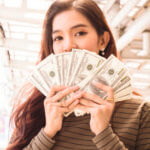 Woman fanning hundred dollar bills up by her face