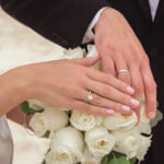 Man and woman's hands showing wedding rings on top of white roses