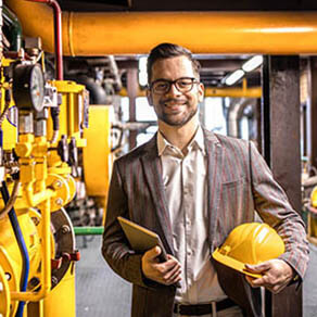 Portrait of young factory manager standing by gas pipeline inside refinery plant.