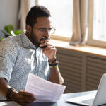 Focused businessman holding documents looking at laptop doing research