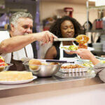 Kitchen with two people Serving Food In Homeless Shelter