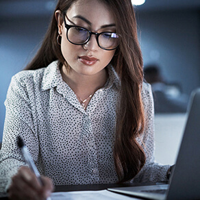 Woman in glasses in a dimly lit room writing on a piece of paper