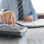 Man sitting at desk with reports, hand working a calculator, charts and stripped tie
