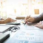 Business man and woman working on financial information the lady is on a calculator and man holding pen with black glasses on desk