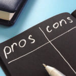 Black paper with white marker writing out the words "pros" and "cons"