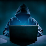 Hacker in the dark in hooded sweatshirt using a laptop