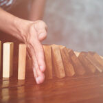Hand stopping domino effect wooden blocks on wooden table