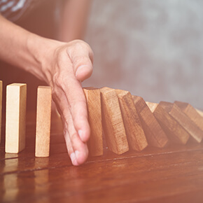 Hand stopping domino effect wooden blocks on wooden table