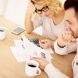 A woman and man reviewing papers, coffee cup, calculator and cell phone on top of a table