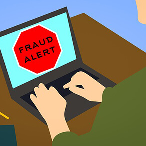 Computer on table, hands typing on keyboard, black letters saying fraud alert on a red octagon