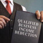 Close up of man in a suit pointing to a book reading, "Qualified Business Inclome Deduction" on the cover