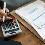 Close-up view of a woman's hand using a calculator and pen adding an invoice