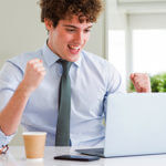 Man excited looking at a computer, with paper cup
