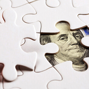 Pieces of jigsaw puzzle with a $100 bill underneath the missing piece.