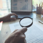 man using magnifying to review balance sheet