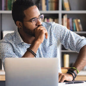 Man sitting in front of a laptop resting his fist on his chin and looking to his left concerned