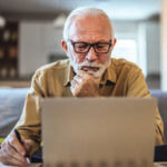 Older man looking closely at a computer screen with his hand resting on his chin