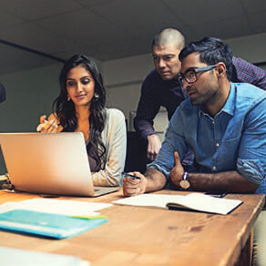 Three coworkers looking over a laptop at a table