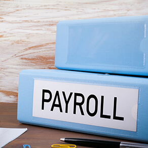 Light blue binders stacked on each other, lower binder has the word payroll on the side