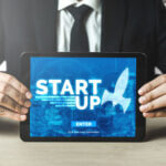 Close up of man in suit holding a tablet computer with a graphic on the screen that reads start up