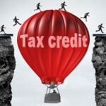 Red hot air balloon with words tax credit between two cliffs with people running over the top