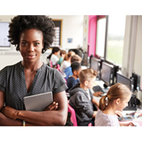Woman facing front in classroom with students working in background
