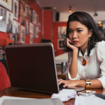 A lady sitting at a table looking at a computer laptop, room painted red with pictures on the wall