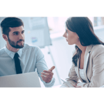 A man and woman talking at a desk with a laptop